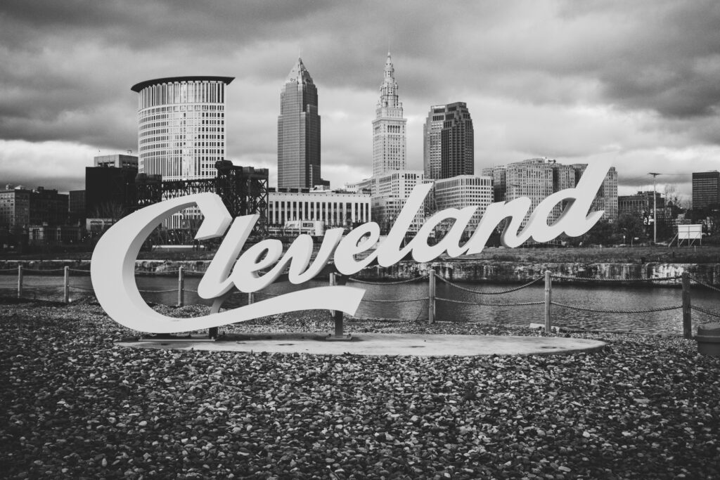 A black and white image of the Cleveland sign in front of downtown Cleveland.